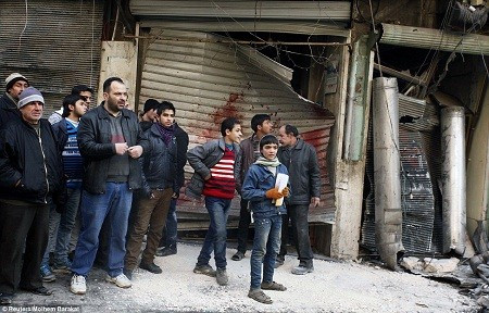 Những người dân đang đứng trước một tấm cửa kéo dính đầy máu sau một vụ không kích vào khu dân cư ở thành phố Aleppo.