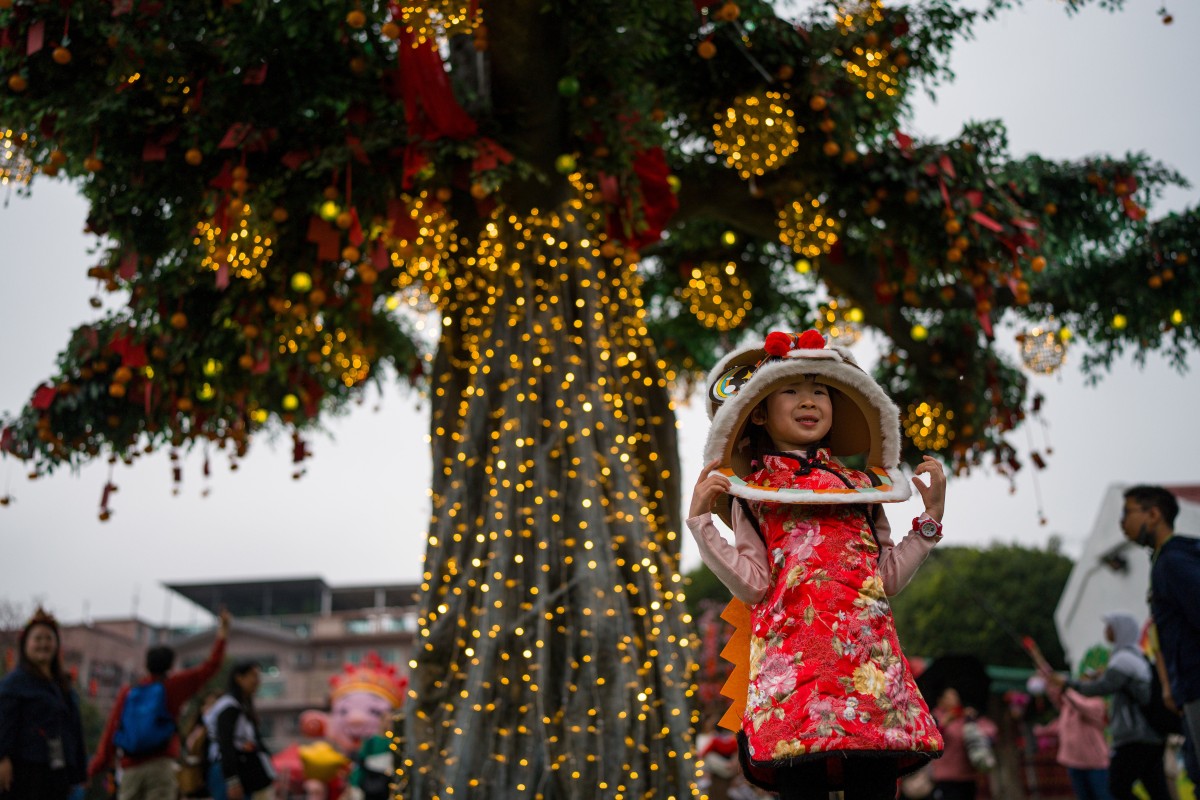 Bé gái mặc trang phục múa lân đứng trước cây ước nguyện ở làng Lam Tsuen, Hong Kong. Vào ngày đầu năm, người dân viết điều ước lên giấy đỏ hoặc thẻ gỗ, buộc vào quả quýt hoặc vật nặng nhỏ rồi ném lên cổ thụ này. Nếu vật đó mắc trên cành, người ta tin rằng điều ước sẽ thành sự thật.