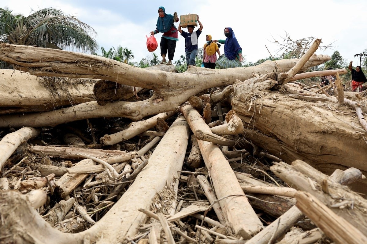 Người dân bước qua những thân cây bị nước lũ cuốn trôi sau mưa lớn tại Karang Baru, tỉnh Aceh, Indonesia, ngày 6/12. Cơ quan ứng phó thiên tai Indonesia cho biết tính đến ngày 6/12, 908 người thiệt mạng và 410 người mất tích vì lũ lụt xảy ra ở ba tỉnh Aceh, Bắc Sumatra và Tây Sumatra trên đảo Sumatra.