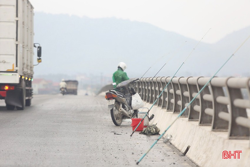Bất chấp các phương tiện giao thông qua lại đông đúc với tốc độ cao, nhiều &quot;cần thủ&quot; vẫn say mê với thú vui câu cá. Xung quanh họ, nhiều chiếc cần câu, thùng đựng mồi, xe máy được để lộn xộn. (Ảnh chụp vào sáng 18/12).