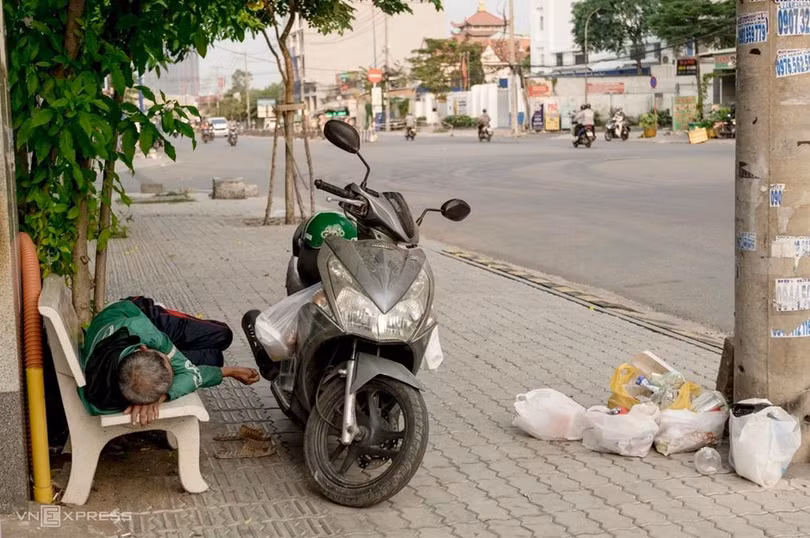 Một tài xế luống tuổi nằm nghỉ trên ghế đá, hộp đồ ăn vẫn treo ở xe. Ảnh: Hoàng Việt.