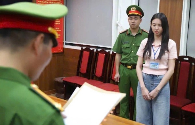 Hoa hậu Thùy Tiên (phải) nghe cảnh sát đọc lệnh khởi tố, bắt tạm giam, ngày 19/5. Ảnh: Bộ Công an