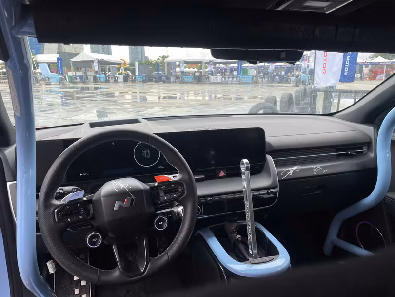 Khu vực táp lô nổi bật với màn hình trung tâm kéo dài, nối với đồng hồ tốc độ. So với mẫu xe tiêu chuẩn, Ioniq 5N phiên bản này được trang bị thêm cần phanh tay ở khu vực yên ngựa, nhằm tối ưu khả năng drifting của người lái.