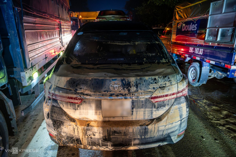 Chiếc Corolla Altis phủ kín bùn đất đang được kéo về gara. Bùn đất màu vàng đã phủ gần kín lớp sơn sẫm màu.