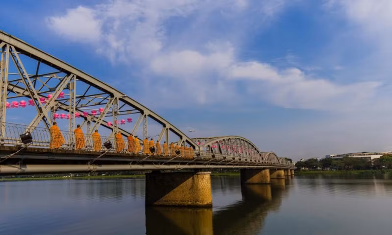 Các sư thầy của chùa Huyền Không Sơn Thượng bước qua cầu Trường Tiền trên đường đi khất thực. Nằm ngay giữa thành phố Huế, đây là cây cầu đầu tiên bắc qua dòng sông Hương thơ mộng, được thiết kế theo kiến trúc Gothic, trải qua nhiều lần trùng tu trong lịch sử và xuất hiện trong nhiều tác phẩm thơ ca Việt Nam. Đây cũng là một biểu tượng thu hút du khách của thành phố Huế. Ảnh: Nguyễn Đình Chiến. dau an viet nam tren nhung nhip cau noi doi bo
