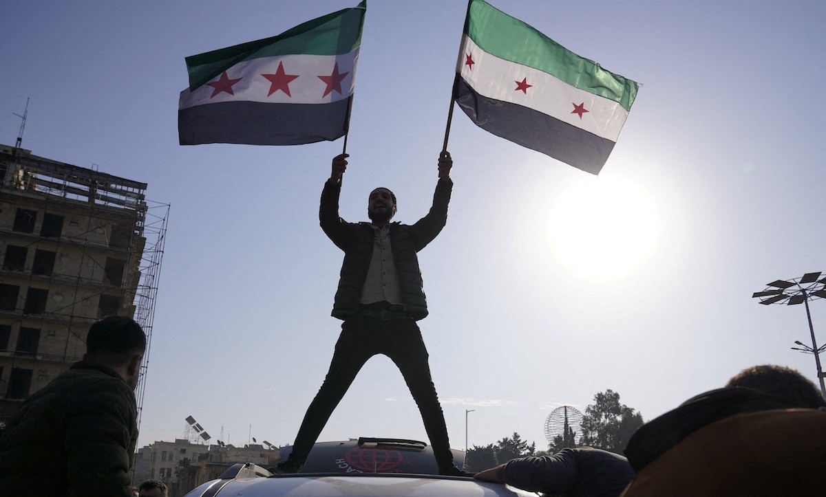Một người đàn ông vẫy cờ của phe đối lập ăn mừng chính phủ Syria sụp đổ ở Aleppo ngày 8/12. Ảnh: Reuters