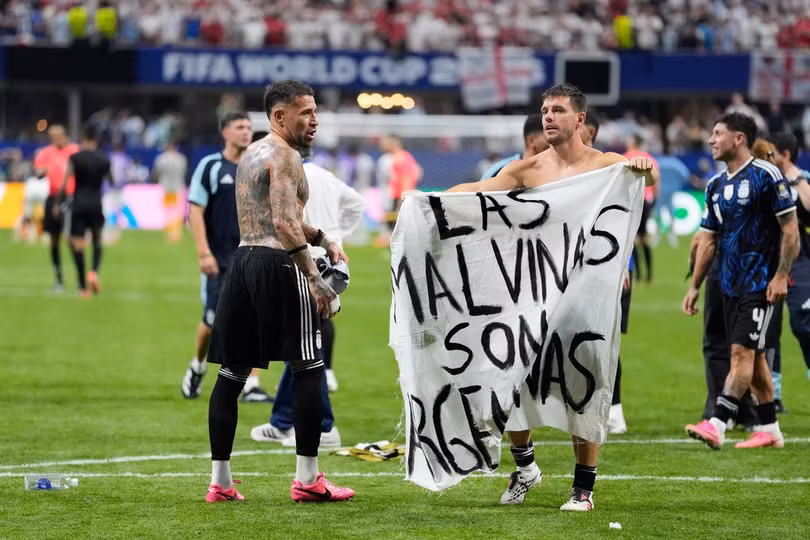Giovani Lo Celso của Argentina cầm biểu ngữ ghi "Quần đảo Malvinas là của Argentina", ám chỉ quần đảo Falklands, trong khi đồng đội Nicolas Otamendi tiến đến sau trận thắng Anh 2-1 ở bán kết World Cup 2026 trên sân Atlanta ngày 15/7. Ảnh: AP
