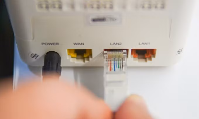 Một người đang cắm dây Ethernet vào modem để kết nối Internet. Ảnh: Lưu Quý
