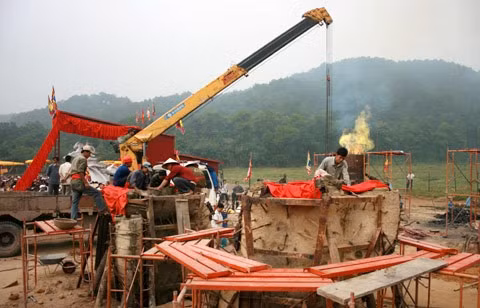 Từ sáng sớm, hàng nghìn người đã đổ về khu đúc tượng cạnh Học viện Phật giáo VN (Sóc Sơn, Hà Nội). Theo lịch âm là ngày "trùng cửu", ngày có ý nghĩa thiêng liêng đặc biệt, rất thích hợp để tiến hành đúc tượng Thánh Gióng - Đức Thánh Phù Đổng Thiên vương. Một mô hình thu nhỏ đặt cạnh khu đúc tượng để phật tử làm lễ, chiêm bái. Khi hoàn thành, tượng cao gần 11 m, độ vươn chéo lên trời khoảng 16 m. Rất nhiều người góp trang sức bằng kim loại quý để hòa cùng dòng đồng nóng chảy lúc đổ vào khuôn. Tại khu đất được cách ly cạnh đó, hai chiếc khuôn của phần đầu ngựa và thân trên Thánh Gióng đang gấp rút được hoàn tất những khâu cuối cùng. Đây là 2 thớt đầu tiên được đúc của tượng đài. Một số chi tiết khác của tượng đài cũng được làm trong mẻ đầu tiên. Hàng trăm thanh đồng đỏ nguyên chất được nung chảy trong lò ga hơn 1.000 độ C. Theo các nghệ nhân, thời gian từ lúc nấu đến lúc đổ đồng mất hơn 2 giờ. Người nghệ nhân cẩn thận trát kín mạch và tạo miệng khuôn để đổ đồng nóng chảy vào. Sau 2 giờ nung, mẻ đồng nóng chảy đổ ra... ... trong khi các nghệ nhân kính cẩn thắp hương mong mọi việc suôn sẻ. Bên ngoài hàng rào, hàng nghìn người chen lấn mong được vào chiêm ngưỡng cận cảnh. Tới dự buổi lễ sáng nay có nguyên Tổng bí thư Đỗ Mười, cùng nhiều vị lãnh đạo. Ngay trước thời khắc 9h9, hòa thượng Thích Thanh Tứ, Phó chủ tịch Trung ương hội Phật giáo VN(người đeo tràng hạt) cùng nhiều quan chức tiến vào khu đúc tượng. Hàng trăm món đồ kim loại quý được thả vào khuôn... ... trước khi dòng đồng đỏ nóng chảy được rót. Theo các nghệ nhân, công đoạn khó nhất của quá trình đúc tượng là khâu làm khuôn: mất 2 tháng. Khuôn phải làm sao để toát lên được thần thái của Thánh Gióng và toàn bộ hoa văn, họa tiết tinh xảo của tượng với đúng tỉ lệ 1:1. Sau khi đổ đầy đồng vào khuôn, cần tới 4 ngày để làm nguội tự nhiên rồi mới phá khuôn.